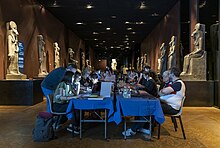 People are seated at tables editing Wikipedia on their laptops in a gallery of Egyptian art