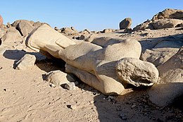 A roughly hewn unfinished statue of a king laying on the ground among rocks.