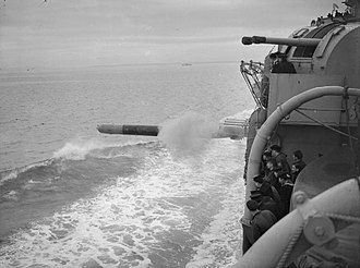 Members of the ship's company watching a torpedo leaving the torpedo tubes mounted amidships during firing trials. One of the cruiser's twin 4-inch gun turrets can be seen. HMS Shropshire torpedo.jpg