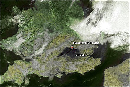 This satellite photo of the south of Britain shows black smoke from the 2005 Buncefield fire, a series of fires and explosions involving approximately 250,000,000 litres of fossil fuels. The plume is seen spreading in two main streams from the explosion site at the apex of the inverted 'v'. By the time the fire had been extinguished the smoke had reached the English Channel. The orange dot is a marker, not the actual fire. Although the smoke plume was from a single source, and larger in size than the individual oil well fire plumes in Kuwait 1991, the Buncefield smoke cloud remained out of the stratosphere.