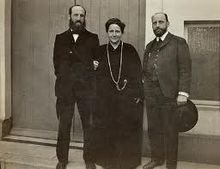portrait en pied : Gertrude Stein habillée en noir est au milieu de ses deux frères, tous les trois regardent l'objectif. l