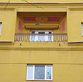 Část žlutého bytového domu s malým balkonem