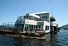 A dirty, futuristic, houseboat-like barge floats amid logs