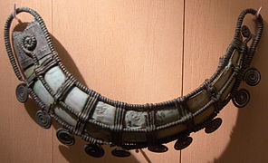 Ornamento (La Colombine, Yonne), ca. 1200 a. C., joya llevada en la cadera, hecha de una malla de bronce decorada con volutas engastando un colmillo de suido, proveniente de una sepultura con enterramiento.