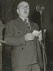 Bir konferansta mikrofona konuşan Tom Garland'ın portresi
