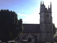 Gray stone building with prominent four stage tower at the right hand end. To the left is a large yew tree.