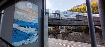 Photographie d'un panneau de soutien de la Région avec la passerelle de Francoz qui enjambe la route départementale 1006.