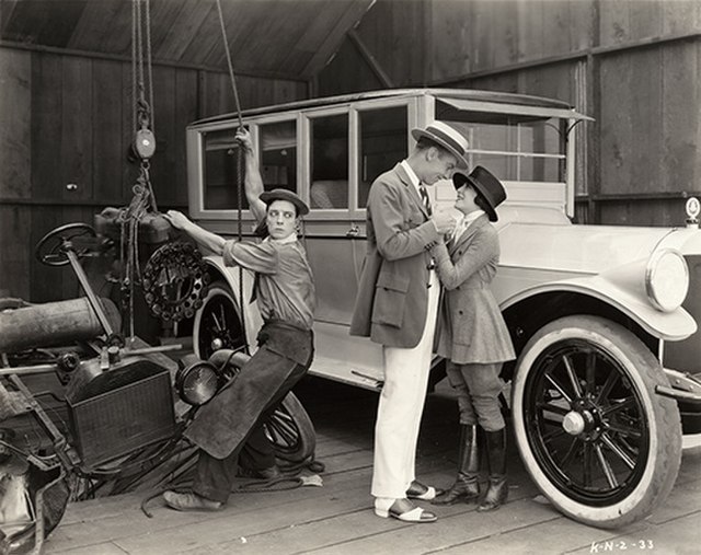 Comedic actor Buster Keaton (left) struggling with a wrecked Model T car in The Blacksmith, a 1922 short comedy film
