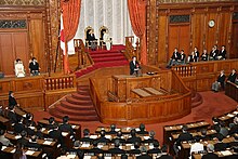 Emperor Akihito and Empress Michiko seated in the Chamber of the House of Councillors of the National Diet, with members of the Imperial Family, the Cabinet, and Prime Minister Naoto Kan giving the government's speech in front of the assembled members of parliament (2010). 20101129gikai1.jpg