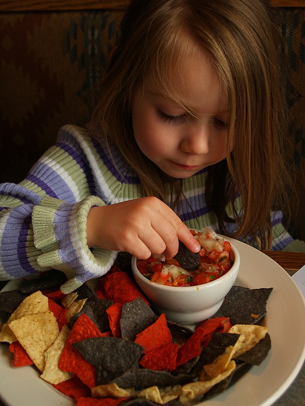 A young girl eating tortilla chips with pico de gallo