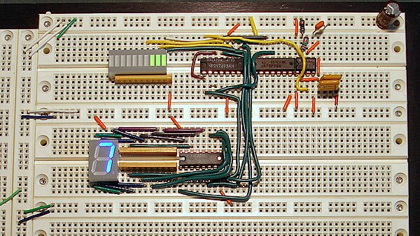 An operating prototyped circuit on a solderless breadboard incorporating four DIP ICs, a DIP LED bargraph display (upper left), and a DIP 7-segment LE