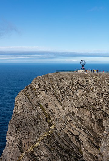 Vista do globo do Cabo Norte, Noruega. A atração turística popular é o ponto mais ao norte da Europa que pode ser acessado de carro. O cabo inclui um penhasco de 307 metros de altura com um grande platô plano no topo, onde os visitantes, se o tempo permitir, podem observar o Sol da meia-noite e as vistas do mar de Barents ao norte. O Salão do Cabo Norte, um centro de visitantes, foi construído em 1988 no platô. Ele inclui uma cafeteria, um restaurante, uma agência dos correios, uma loja de souvenirs, um pequeno museu e um cinema com vídeo. (definição 5 149 × 5 149)