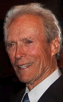 A headshot of an older man is looking to the left while smiling