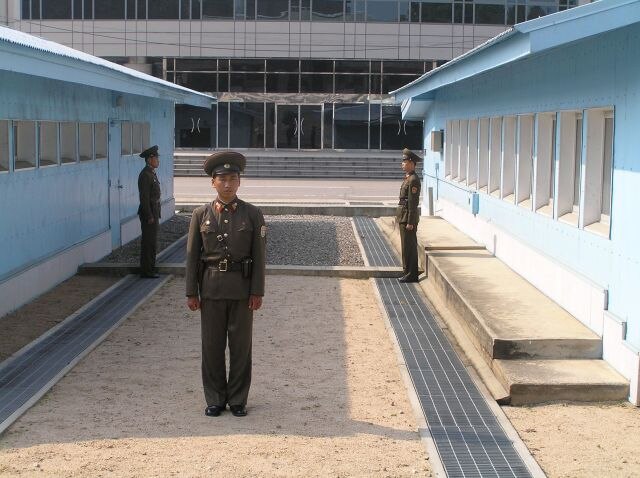 North Korean soldiers standing guard at the JSA between the blue buildings. View from the north. To the rear, the ground floor of Freedom House, in So