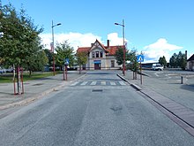 Foto einer Straße, die auf ein Bahnhofsgebäude hinführt