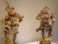 Dřevěné figurky šklebících se ozbrojenců ve zdobné zbroji, vybledlé barvy (hnědá a šedá)