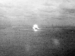 Photographie en noir et blanc lointaine où on distingue l'explosion du navire.
