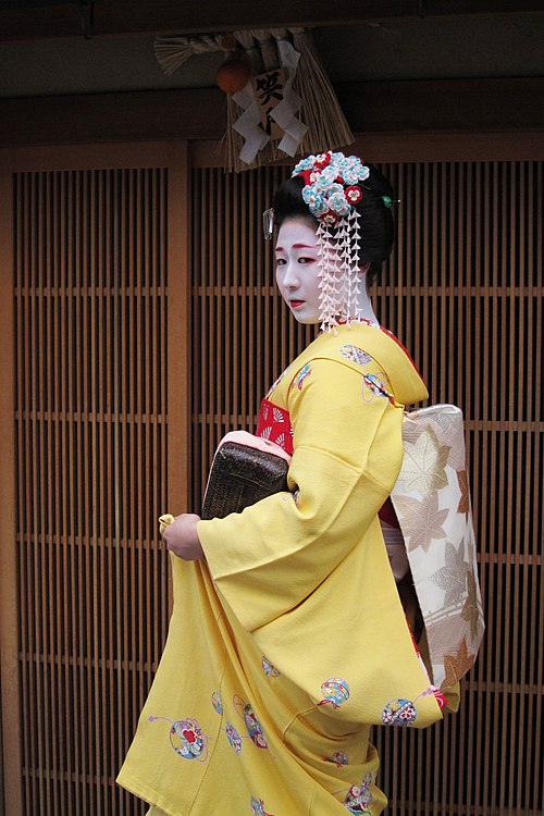 Minarai Katsunosuke wearing a short obi and a large, colourful set of kanzashi hairpins