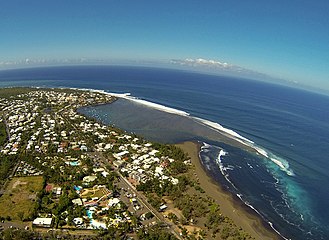 Ein schwarzer Sandstrand, an dem ein Riff große Wellen erzeugt, die zum Surfen geeignet sind.