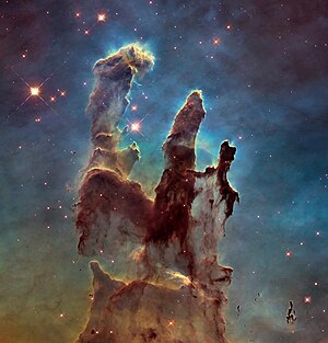 עמודי הבריאה כפי שצולמו על ידי טלסקופ החלל האבל ב-2014. התמונה נוצרה מהלחמה של שלוש תמונות בצבעים שונים. "עמודי הבריאה" הם אזור בערפילית הנשר - צביר פתוח של כוכבים בקבוצת הכוכבים זנב הנחש. האזורים האפלים הם עננים מולקולריים ודסקות קדם פלנטריות המקיפות קדם-כוכבים.