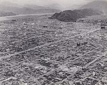Black and white photo of a destroyed urban area. The outline of a grid pattern of streets is visible, but most buildings have been reduced to rubble.