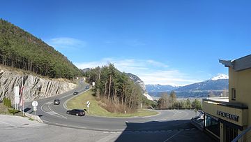 Haarnadelkurve der Zirlerbergstraße, dahinter die Martinswand und das Inntal mit am Horizont befindlichen Tuxer Alpen