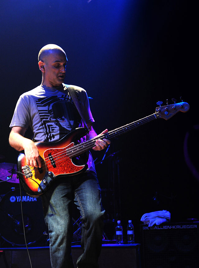 A photograph of a man playing the guitar on stage. He is wearing a t-shirt and jeans.
