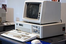 Ein Foto eines 1980er-Jahre Computers mit Monitor, Tastatur und Maus auf einem Schreibtisch.