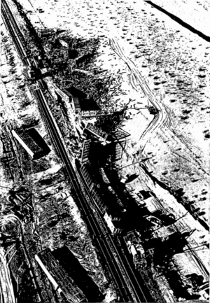 A black-and-white view of a train wreck. Several completely destroyed railcars are strewn about a sea of crossties near the top of the image, with a number of less-destroyed railcars snaking down to the caboose near the bottom of the image.