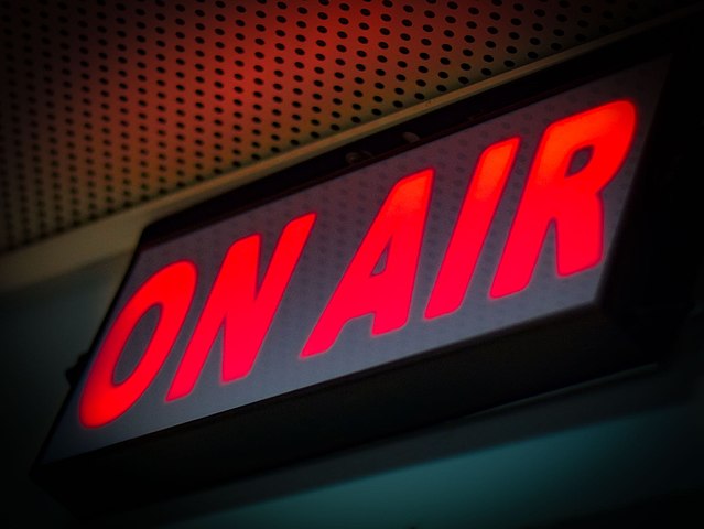 An "On Air" sign is illuminated, usually in red, while a broadcast or recording session is taking place.