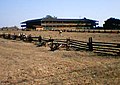 Açık çayırların ortasında geniş verandalara sahip geniş, alçak, iki katlı bir bina olan Petaluma Adobe'nin fotoğrafı.