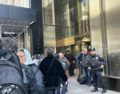 A photograph of a crowd of people standing outside of Trump Tower. NYPD officers are dispersed in the crowd.