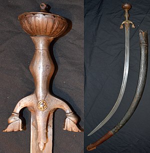 Afghan pulwar, 19th century mounts, earlier (17th to 18th century) deeply curved 82 cm blade of damascus watered steel, inlaid on one side with maker's mark and Islamic inscription, other gold inlays throughout the blade, large iron hilt with characteristic down turned quillions and brass rivet caps, inside measurement 104 cm, leather over wood scabbard with iron chape. Z pulwar hilt.jpg