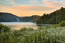 Photographie d'un petit lac entouré de collines recouvertes de forêts au moment de l'heure dorée.