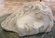 Un busto de la cabeza de una Erinyes, dormida y acostada de lado.  Tiene rasgos humanos y cabello normal.