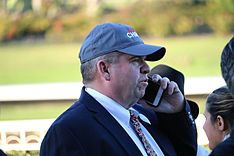 un homme d'âge moyen dans un costume sombre et une casquette de baseball, parlant sur un téléphone portable