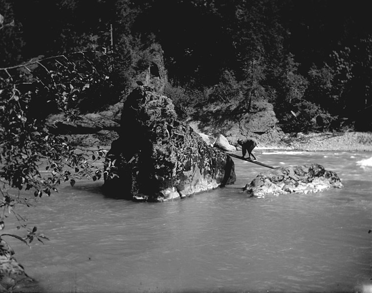 File:Man climbing toward rock in river (3945319149).jpg