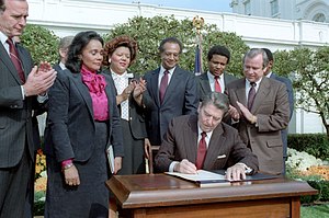 Ronald Reagan at the signing ceremony for Martin Luther King Jr. Day legislation in the Rose Garden. Coretta Scott King, George H. W. Bush, Howard Baker, Bob Dole, Jack Kemp, Samuel Pierce, and Katie Hall looking on.