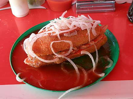 Mexican torta ahogada, a pork sandwich with chili/tomato sauce, onion slices and lime juice