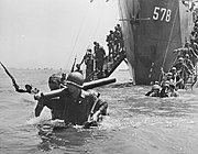 Men wearing military uniforms and carrying equipment walking down ramps from a ship into the sea