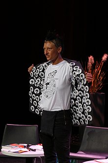 Réédition de la performance Makita free Angela avec le t-shirt  Stop Sexism on Wikipedia pendant la Wikiconvention francophone de 2016, à la Halle Pajol de Paris (photo d'une amatrice prise pendant la performance)