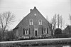 Boerderij, waarvan het woongedeelte een afgeknotte puntgevel met sierankers heeft en links een opkamer. Hogere houten stal onder een rieten dak met het woongedeelte