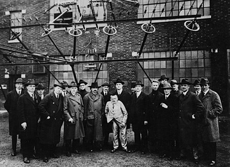 A 1921 photograph of Albert Einstein being given a tour of The New Brunswick Marconi Radio Station in Somerset, New Jersey (then part of RCA) along with RCA officers and leading scientists and engineers in the electrical and radio fields from RCA, General Electric, American Telephone and Telegraph, and Western Electric. The feedlines feeding radio power from the transmitter to the huge flattop wire antenna are visible, top. Albert Einstein with other engineers and scientists at Marconi RCA radio station 1921.jpg
