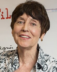 Portrait souriant d'une femme brune aux yeux gris, d'un certain âge, coupe au carré.