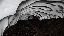 This glacier cave has been excavated by a hot spring underneath a snow field in south central Iceland, a country where such formations are common due to the high geothermal and volcanic activity, plus the high latitude, cold weather, and frequent snowfall. Cueva excavada en el hielo por aguas termales, Islandia.JPG