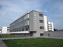 Photographie en couleur d’un bâtiment vu de trois-quart. Béton et façade en baies vitrée.