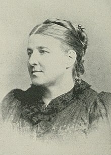 B&W portrait photo of a woman with blonde hair in an up-do, wearing a dark blouse.