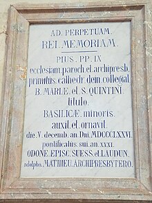 Plaque de marbre accrochée à un mur de pierre. Des phrases en latin y sont gravées.