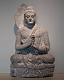 Buda assegut, Gandhara, c. segle IV e.c.. Apart de poder guaitar la major part dels detalls anteriorment esmentats, s'hi pot observa fragmentàriament l'aurèola en la part posterior.