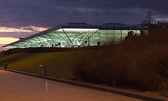 The large, white Stansted Airport terminal building lit up at dusk, against a blue and purple sky.